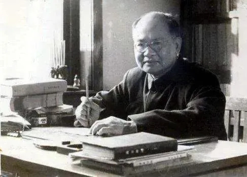 图片为王力先生的黑白照片，他坐在书桌旁，桌上摆放着书籍、文具等物品，背景有书架。王力是中国现代语言学的奠基人，文中提到他讲的“用英文的句子骨架说中文”是欧化中文的重要来源，强调“用词洋气”不算欧化中文，只有套用英文句子骨架才叫欧化中文，如“他昨晚睡得很晚”写成“他是很晚才睡的”即为欧化。