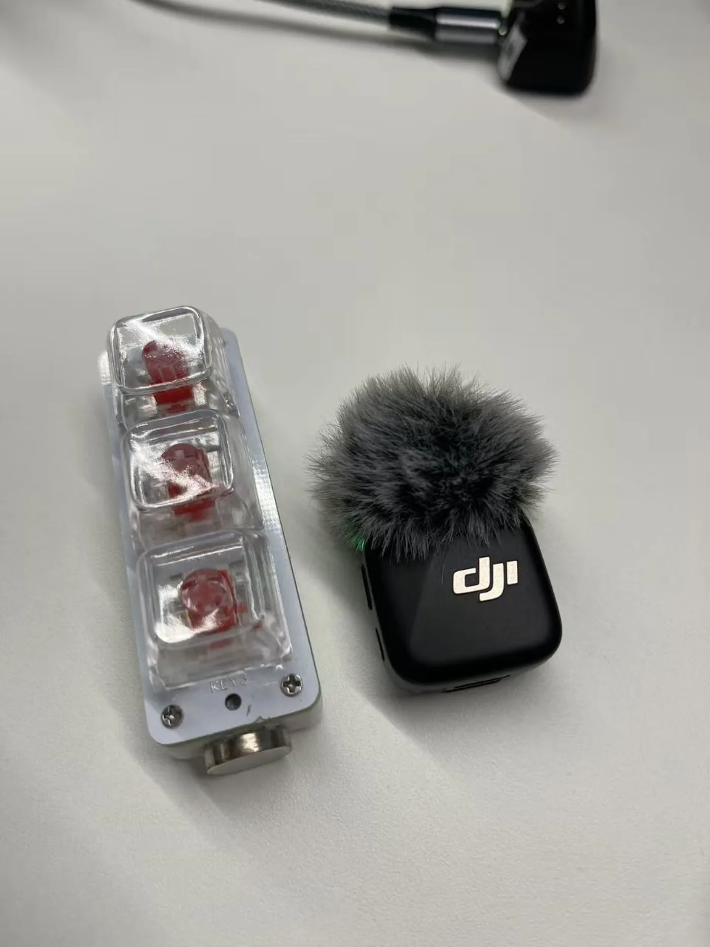 图片展示了两款设备。左侧为透明塑料外壳的设备，内有红色晶体，底部有金属接口。右侧是黑色设备，表面有“dji”标志，顶部装有灰色毛绒防风罩。这两款设备可能是用于语音输入的辅助工具，与文档中提到的语音输入设备相关，可能用于实践中的语音输入场景。